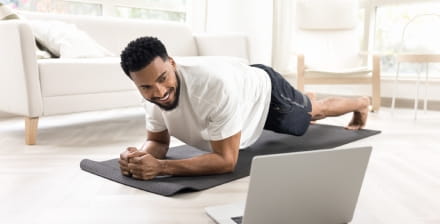 Homem jovem faz exercício em casa seguindo uma aula online.