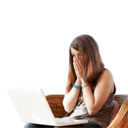 Mulher jovem sentada, com portátil sobre joelhos, a olhar para ecrã com mãos no rosto